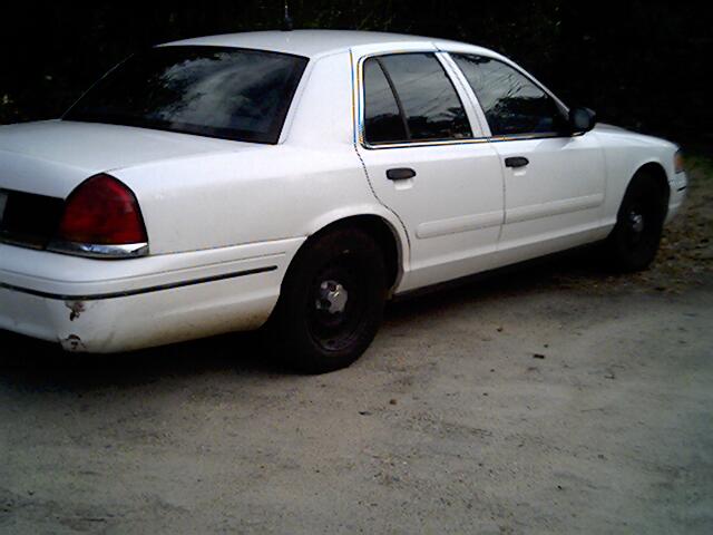 White four-door sedan viewed from rear passenger side on gravel lot