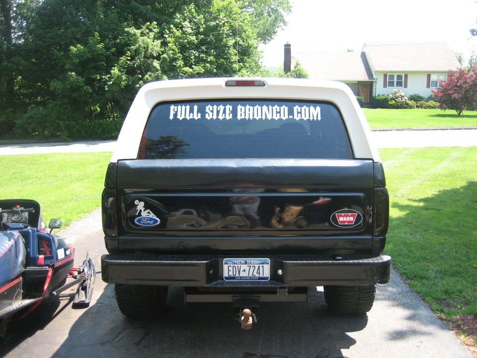 Rear view of a black Ford Bronco with a white top. It has a 'FULL SIZE BRONCO.COM' sticker on the rear window and a Ford logo sticker on the tailgate