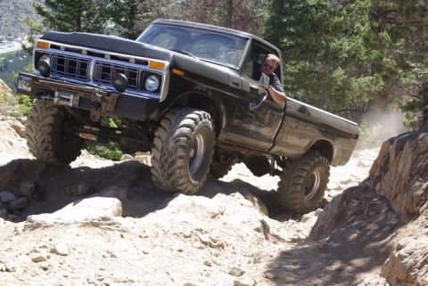 1995 Ford Bronco - A modified black 1977 Ford F-150 navigates a challenging rocky terrain, kicking up dust as it climbs.