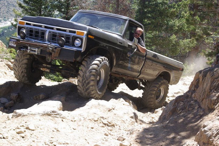 Lifted dark green 1970s Ford 4x4 pickup on big mud tires climbing rocks on a mountain trail