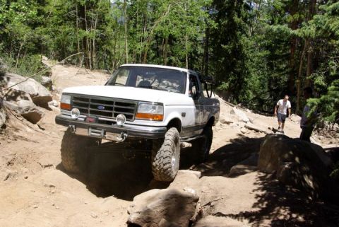 1995 Ford Bronco - Ford Bronco tackles a challenging off-road path in a forest setting.
