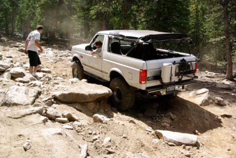 1995 Ford Bronco - A white SUV navigates a challenging rocky trail in a wooded area.