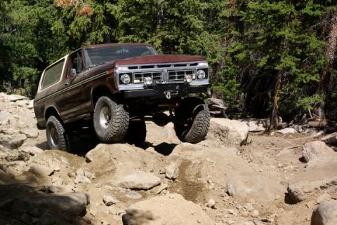 1995 Ford Bronco - A vintage Ford Bronco navigates a challenging rocky terrain in a wooded area.