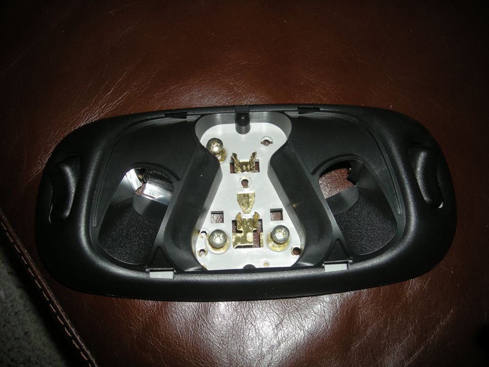 Black plastic interior light assembly with metal bulb sockets and screws, resting on a brown textured surface