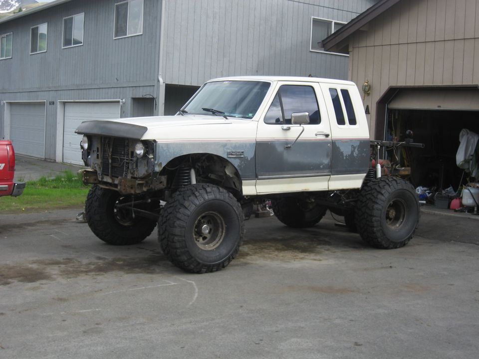 White and gray lifted 1990 Ford F-250 with large off-road tires parked in driveway