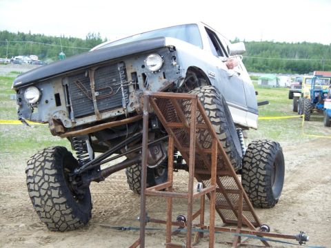 1990 Ford F-250 - A heavily modified pickup truck is positioned on a metal ramp, its large off-road tires and lifted suspension.