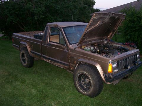 1993 Jeep Cherokee - A brown Jeep pickup truck sits on grass with its hood open, revealing the engine.