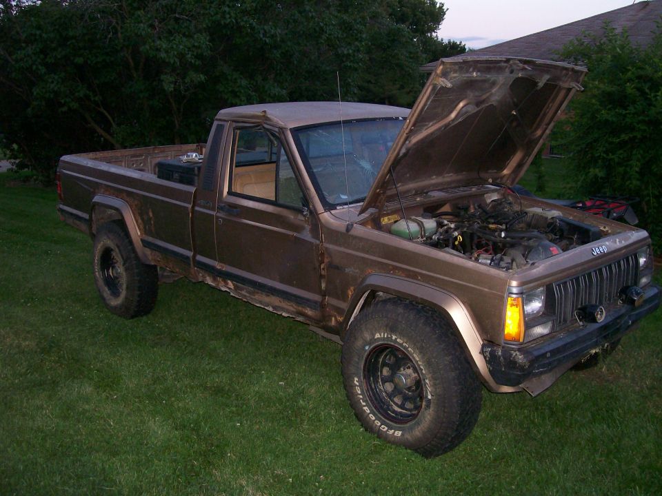 Brown Jeep pickup truck with hood open, parked on grass