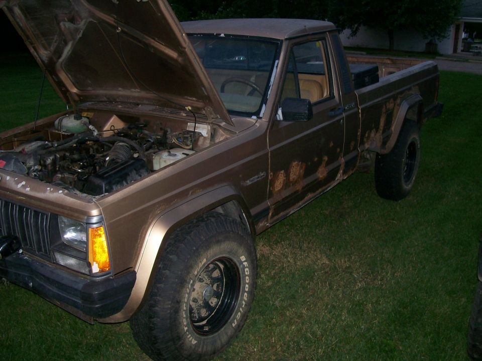 Brown Jeep Comanche pickup truck, hood open, showing engine. Rust on lower body panels