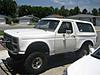 1986 Ford Bronco - A white 1980s Ford Bronco with a lifted suspension is parked in a residential area.