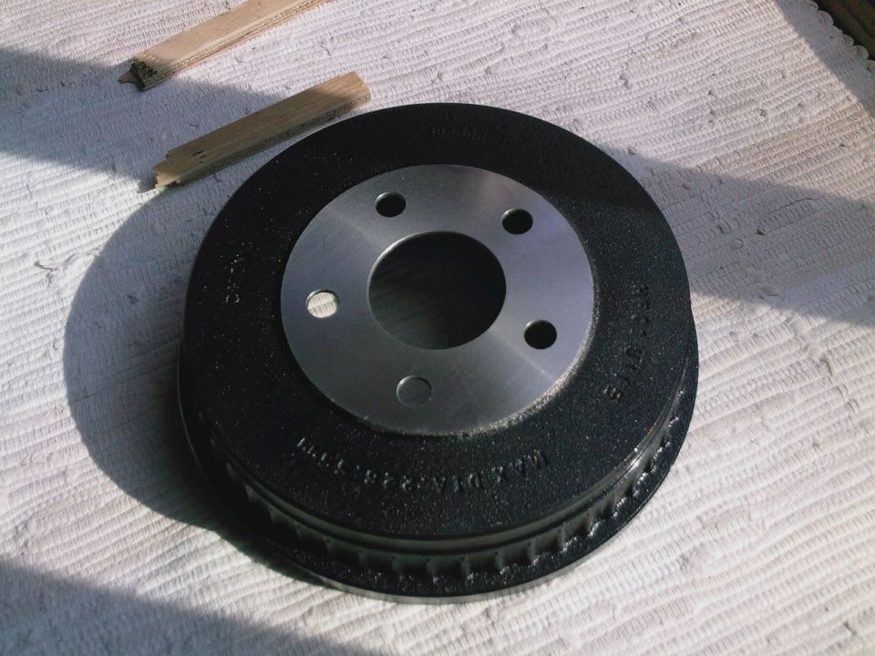 New black brake drum with machined center and four lug holes resting on a white blanket