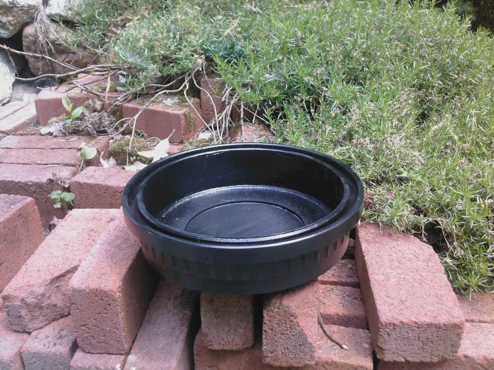 Black engine oil pan or housing component sitting on a brick stack outdoors