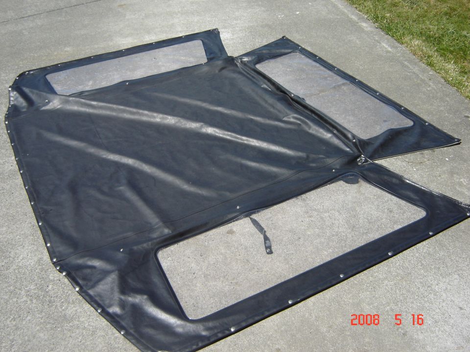 Black soft top with clear plastic windows laid out on concrete