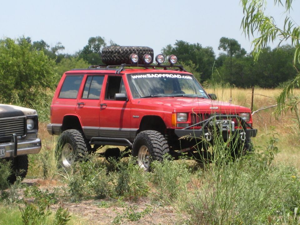 Red Jeep Cherokee XJ with roof rack, spare tire, and off-road bumper