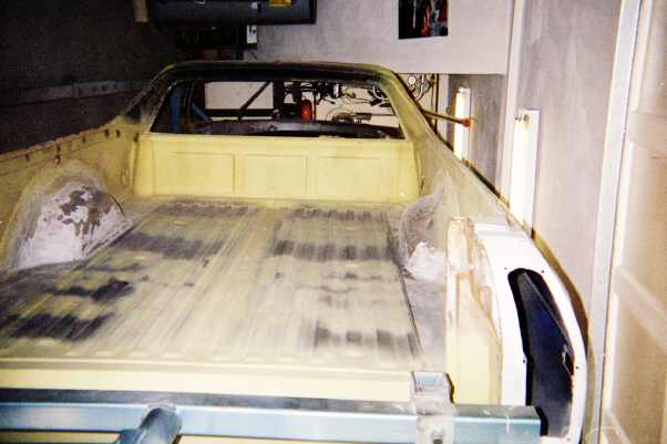 Stripped pale-yellow muscle car body shell on a frame in a garage
