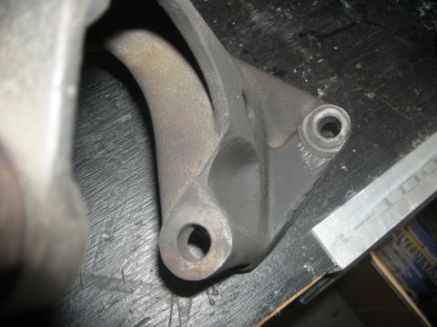 1986 Ford Bronco - A close-up view of a metal bracket with a curved arm and two mounting holes.