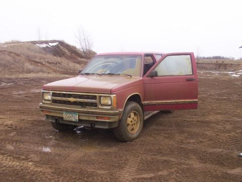 1972 Pontiac Grand Prix - This red pickup truck is parked in a muddy area. The driver's side door is open.