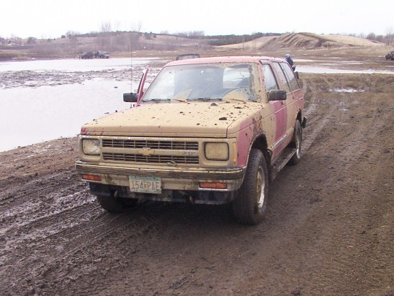 Mud-covered tan and red Chevrolet S-10 Blazer SUV parked on a muddy off-road lot