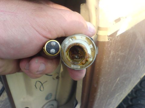 1986 Ford Bronco - A hand holds a corroded light bulb socket and a two-pin bulb, with a portion of a tan vehicle visible.
