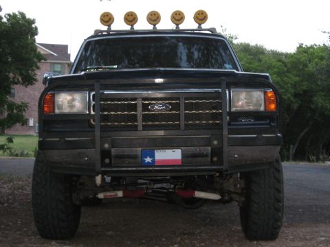 1990 Ford Bronco - Front view of a lifted black Ford pickup with a tubular grille guard, roof-mounted smiley-face off-road lights, and a Texas front license p…