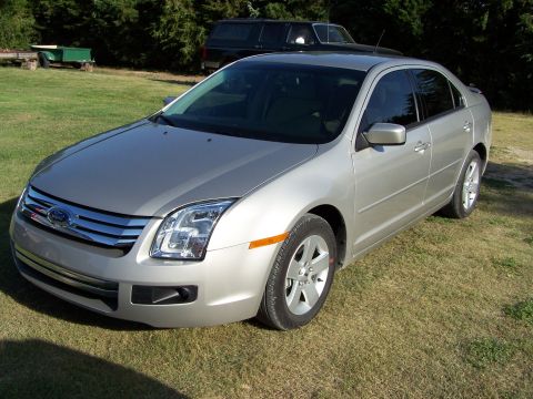 2008 Ford Fusion - A silver sedan is parked on a grassy area with trees and another vehicle in the background.