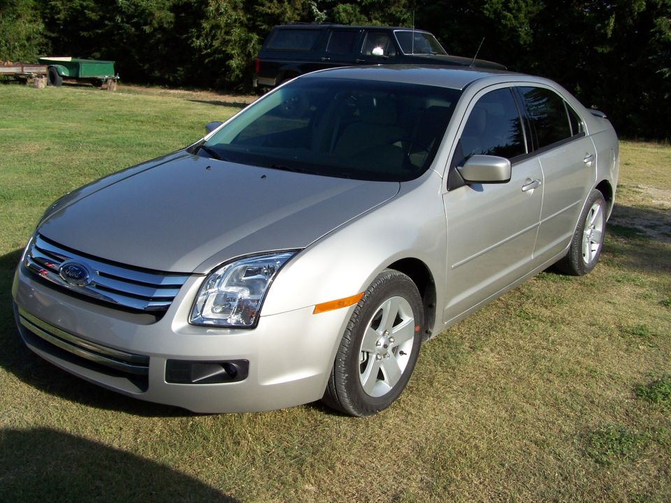 Silver Ford Fusion sedan parked on grass with a trailer in the background