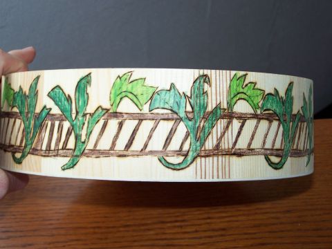 1995 Ford C-350 (Centurion Conversions) - A wooden cylinder decorated with pyrographic art green leaves and a fence pattern is held by a hand.