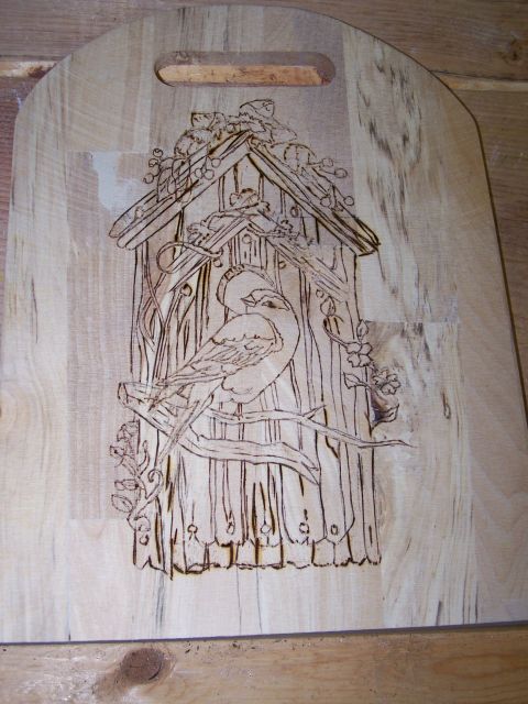 1995 Ford C-350 (Centurion Conversions) - A wooden cutting board features pyrography art depicting a birdhouse with two birds perched on branches.