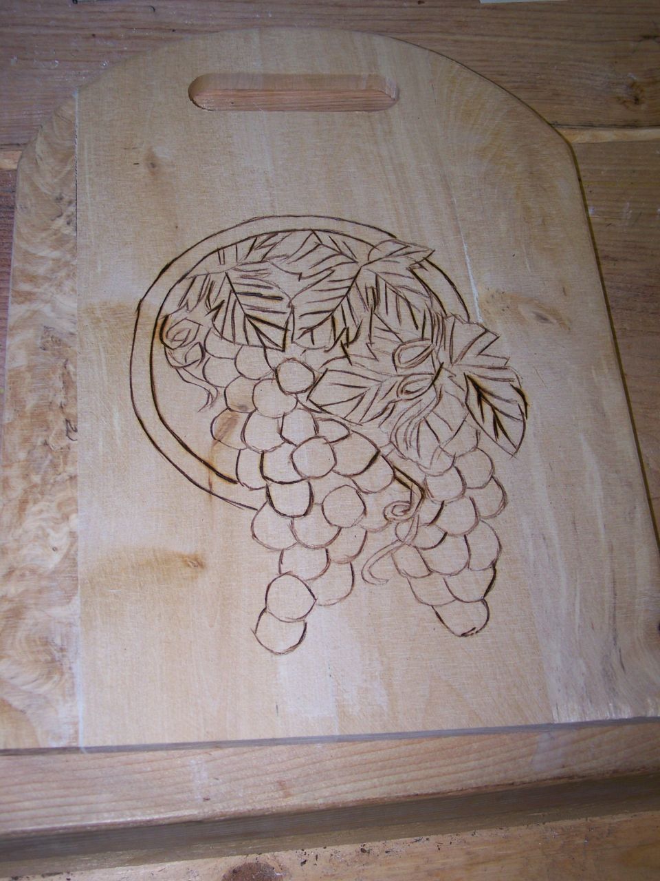 Wood cutting board with unfinished pyrography of grapes and leaves