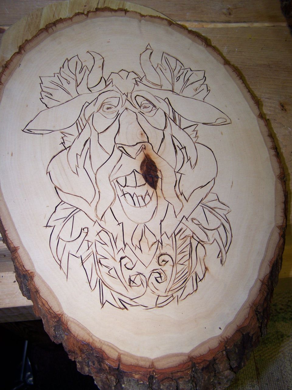 Wood slice with a carved face, possibly a green man, with leaves and horns