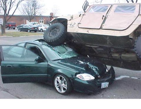 2000 Mercury Grand Marquis - A military vehicle has crushed a green sedan, causing significant damage to the car.