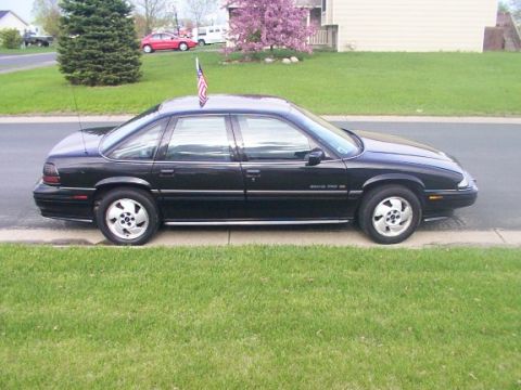 1972 Pontiac Grand Prix - A black sedan is parked on the side of the road with a small American flag on its roof.
