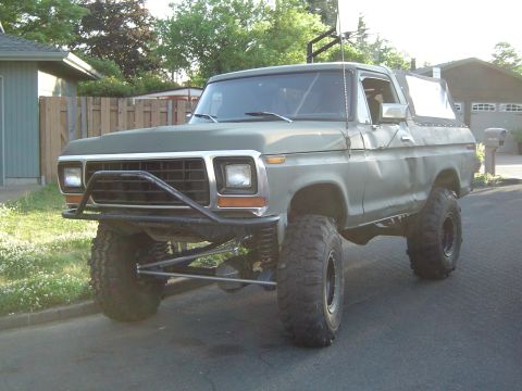 1978 Ford Bronco - Olive green 1978 Ford Bronco with large off-road tires and a brush guard parked on a suburban street.