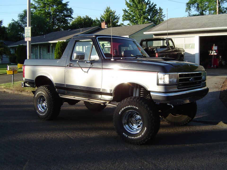 Lifted black and silver Ford Bronco with top removed on BFGoodrich mud tires in a driveway