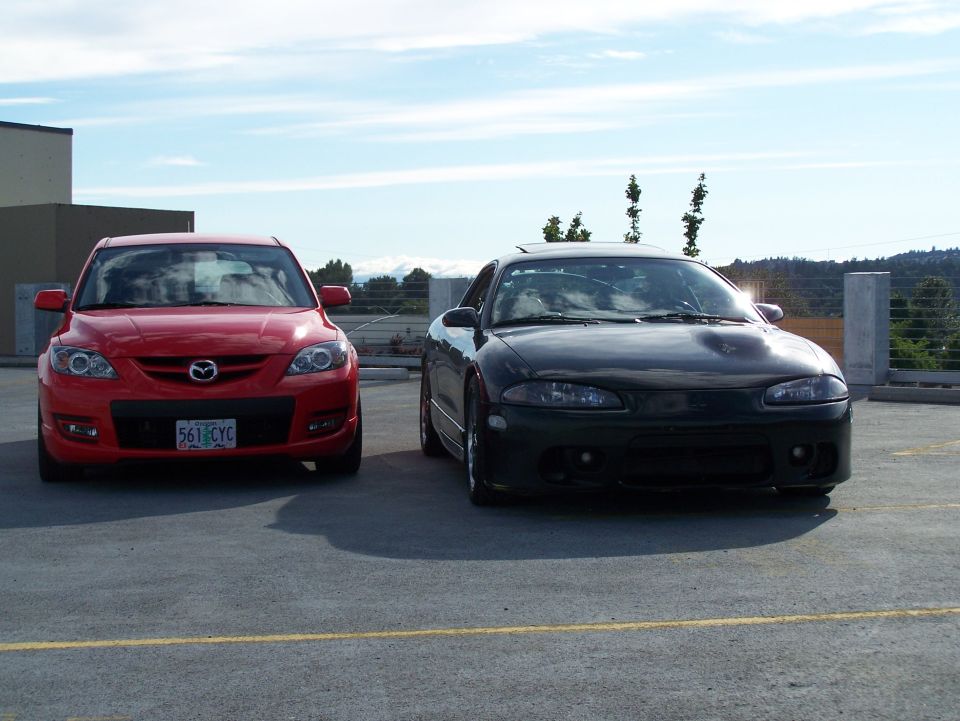 Red 2007 Mazda 3 parked next to a dark coupe, front view