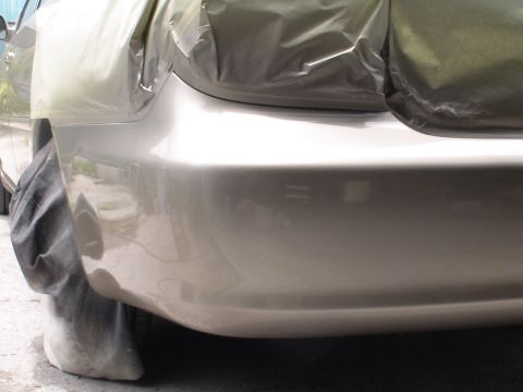 1993 Ford C-350 (Centurion Conversions) - A car's rear bumper and wheel well are covered with protective sheeting and cloth, suggesting preparation for or completion of bodywork.