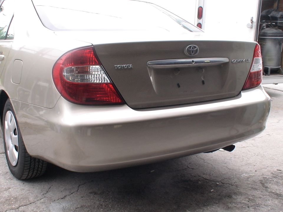 Rear view of a tan Toyota Camry LE sedan. The Toyota logo is on the trunk lid