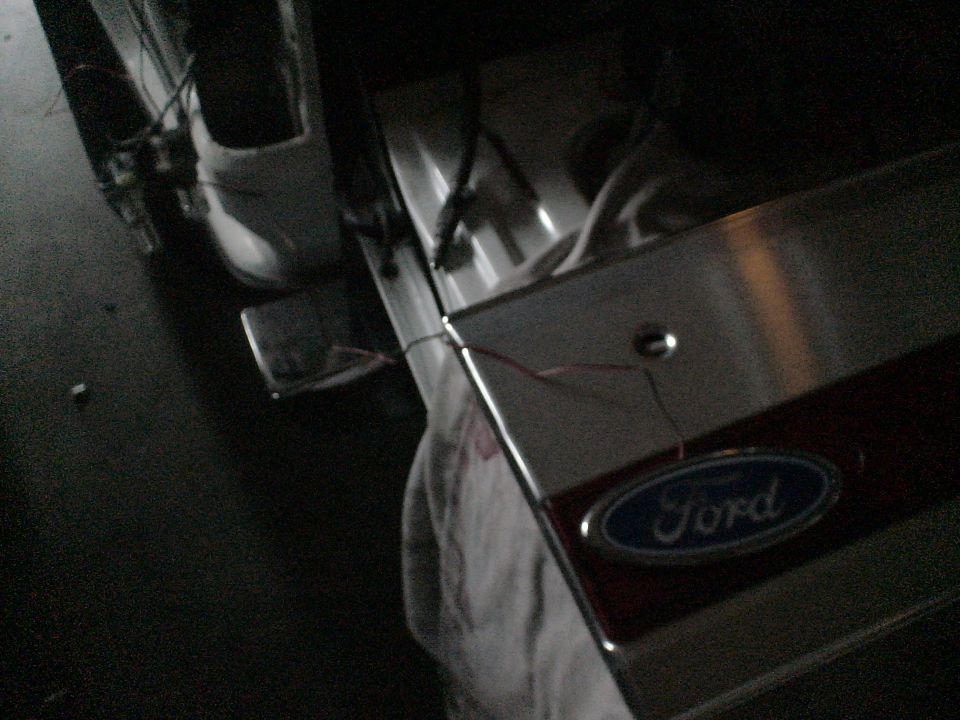 Close-up of a Ford oval emblem on a vehicle's tailgate, with exposed wiring