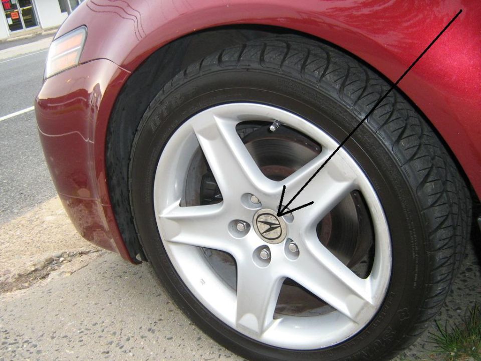 Maroon Acura front wheel with silver five-spoke alloy and center cap, arrow pointing to hub