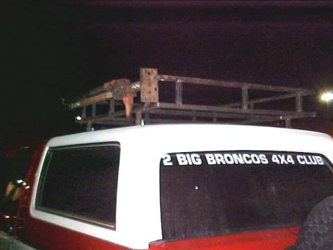 1987 Ford Bronco - A custom metal roof rack is mounted on the top of a red and white SUV, with a club sticker on the window.