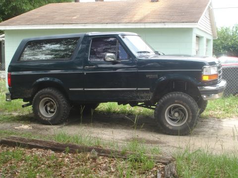 1989 Ford Bronco - This dark green Ford Bronco SUV is shown from the side, lifted with aftermarket wheels.