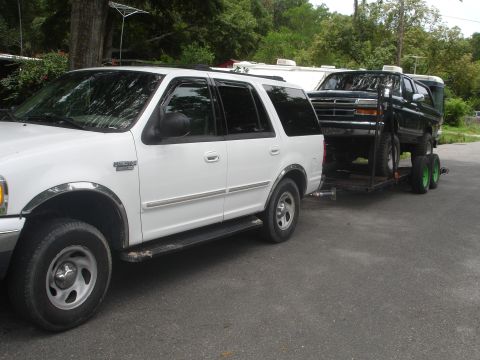 1989 Ford Bronco - A black Ford Bronco is transported on a trailer behind a white SUV.