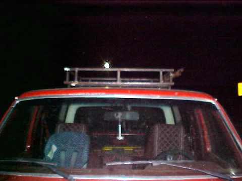 1987 Ford Bronco - The front interior of a red SUV is visible, along with a metal roof rack above. The vehicle appears to be from the 1980s.