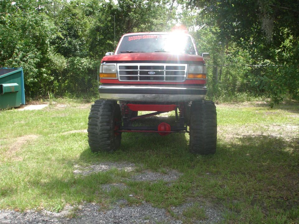 Front view of a red lifted Ford truck with oversized tires and a custom grille