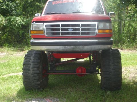 1989 Ford Bronco - This lifted Ford truck features a prominent grille and massive tires, suggesting a model year in the early to mid-1990s.
