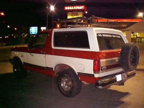 1987 Ford Bronco - Rear view of a two-tone red and white 1987 Ford Bronco with a spare tire and roof rack.