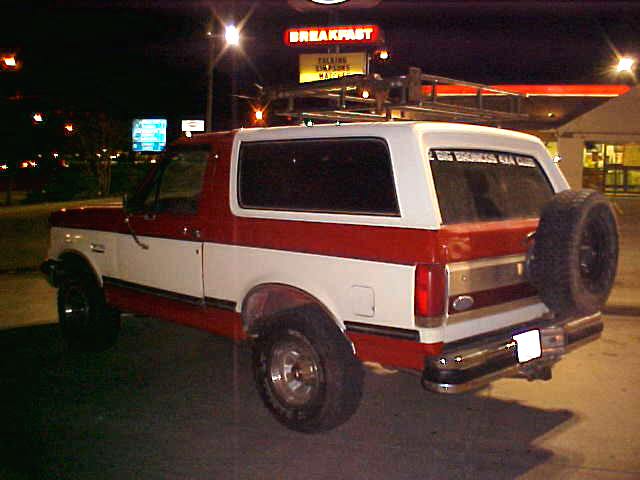 1987 Ford Bronco parked at night, rear view showing spare tire on tailgate and roof rack