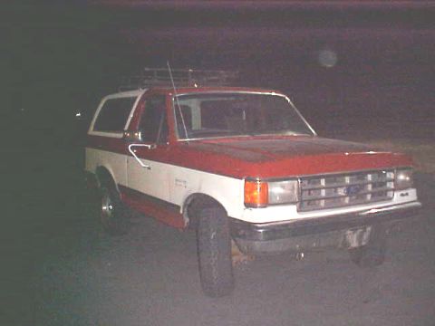 1987 Ford Bronco - This two-tone Ford Bronco is parked outdoors at night, showing its front-right side.