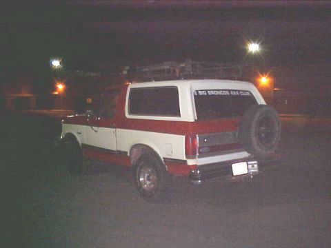 1987 Ford Bronco - This two-tone red and white 1987 Ford Bronco is seen from the rear at night, with a spare tire on the tailgate.
