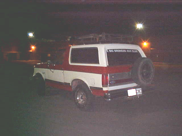 1987 Ford Bronco, two-tone red and white, with spare tire mounted on rear door, parked at night